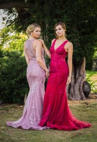 Fishtail Dresses Two women in elegant evening gowns, one in pink and the other in red, pose outdoors.